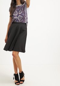 Jupe noire en coupe A associée à un haut à motifs violet et blanc. La tenue présente une coupe décontractée et des bottines noires avec des accents en dentelle.