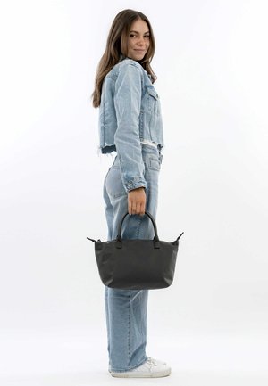 Borsa a tracolla nera con manici arrotondati, realizzata in materiale liscio, con accenti sottili. Il modello indossa una giacca in denim chiaro e jeans.