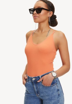 Geribbelde oranje tanktop met dunne bandjes, gecombineerd met hoge blauwe jeans. Accessoires zijn onder andere zwarte zonnebril en een zilveren horloge.