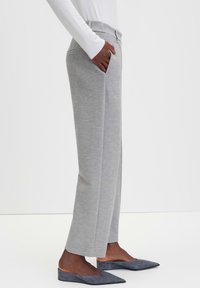 Grijze high-waisted broek met een gestructureerd uiterlijk, voorzien van zijzakken en een rechte pijp, gecombineerd met donkergrijze instappers.