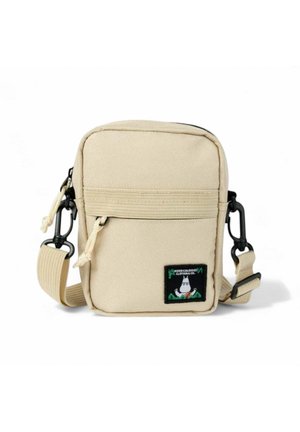 Pieni beige olkalaukku, jossa on edessä vetoketjutila, säädettävä olkahihna ja musta tägi, jossa on valkoinen sarjakuvahahmo.