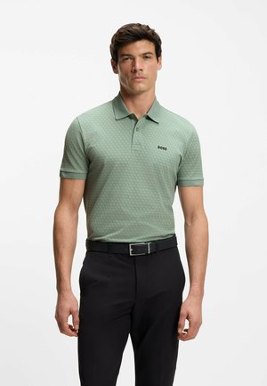 Green polo shirt with a hexagonal pattern, short sleeves, and a collar; features a small black "BOSS" logo. Paired with black trousers and belt.