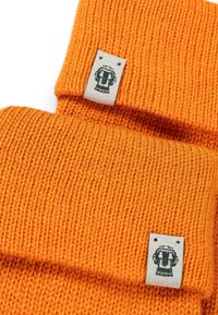 Oranges Strickmütze mit umgeschlagenem Design. Ein Etikett mit grafischen Details ist an der Seite angenäht. Die Textur ist gerippt und dick.