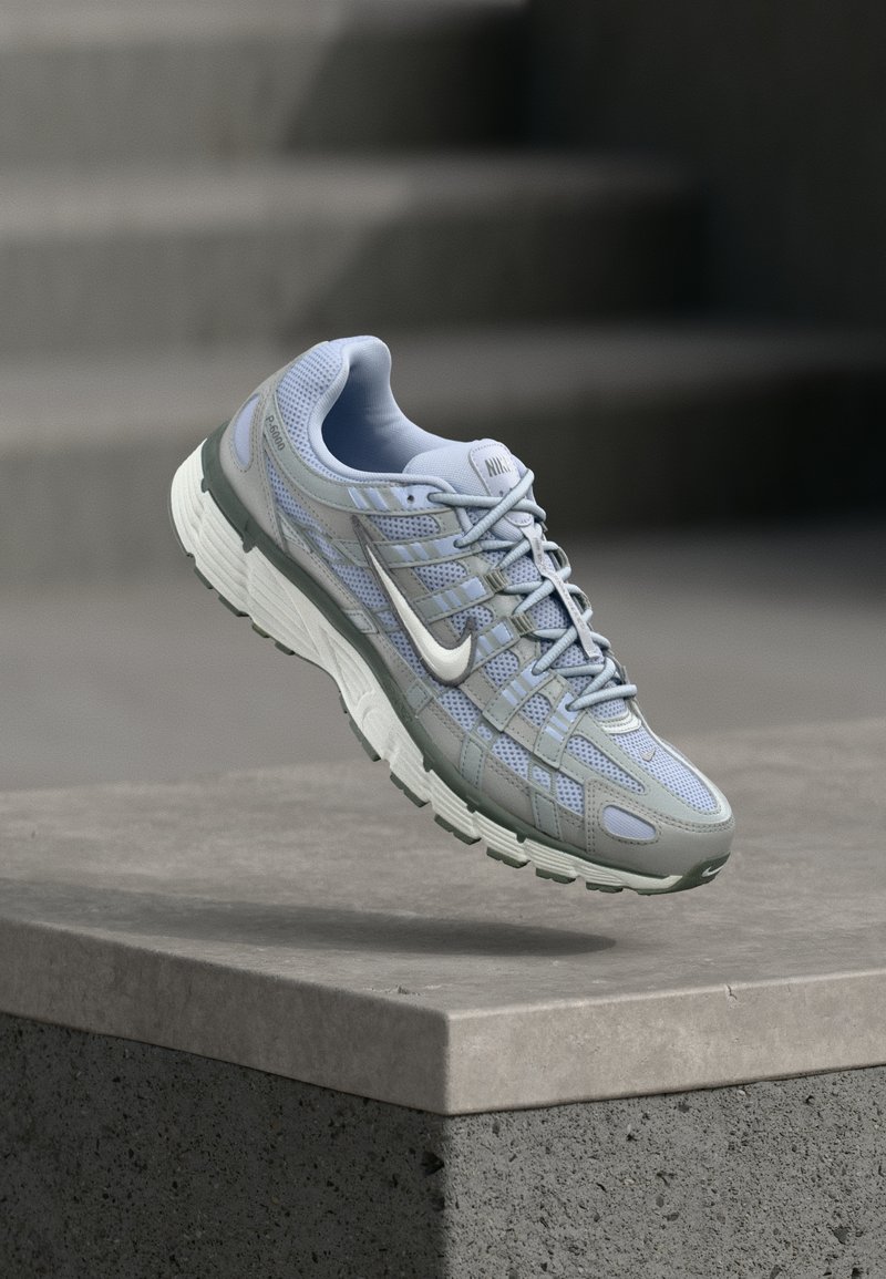 Ανοιχτό μπλε και γκρι αθλητικό παπούτσι Nike αιωρείται πάνω από μια τσιμεντένια άκρη με θολό φόντο σκάλας.