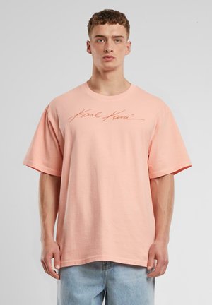 Lyserød oversized t-shirt lavet af bomuld, med et signaturlogo i en kontrastfarve. Korte ærmer, rund halsudskæring, afslappet pasform.