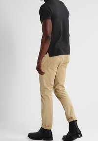 Svart kortärmad skjorta, ljusbeiga byxor och svarta stövlar. Skjortan har en något längre bakre fåll; byxorna har en kroppsnära passform.