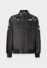 Black racing jacket with grid pattern, featuring green stitching, high collar, and ribbed cuffs. Logos on sleeves and chest. Lightweight material.