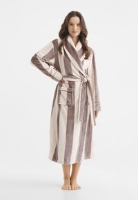 Pasiasty szlafrok z miękkiego, puszystego materiału. Posiada kołnierz typu szal, długie rękawy i zawiązywany pasek. Kolory obejmują jasne i ciemne pasy w odcieniach beżu.