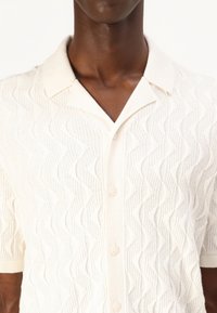 Korte mouwen, crème kleurig overhemd met een golvend textuurpatroon, voorzien van een klassieke kraag en een knoopsluiting met parelmoerachtige knopen.