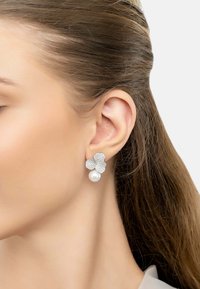 Silver flower-shaped earrings with crystal embellishments and a single white pearl drop. The design is detailed and elegant.