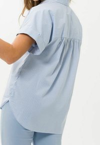 Camicia azzurra a maniche corte con righe bianche, caratterizzata da un design con schiena plissettata e un orlo arrotondato. Tessuto morbido con una vestibilità casual.