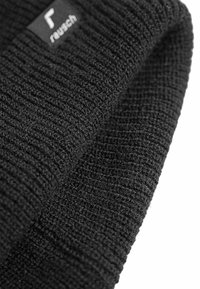 Bonnet en tricot noir avec un motif texturé, comportant une petite étiquette de marque. Le matériel semble doux et flexible, adapté aux temps froids.