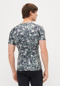 Tæthed tilpasset atletisk skjorte i camouflage mønster, med nuancer af grå og grøn, korte ærmer og et glat, strækbart stof. Logo på ryggen.