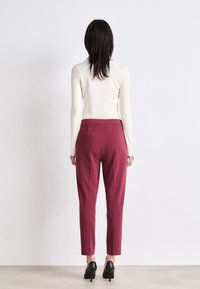 Strak aansluitend crèmekleurig topje en hooggesneden bordeauxbroek met een taps toelopende pijp; gecombineerd met zwarte hakken. Minimalistisch ontwerp.