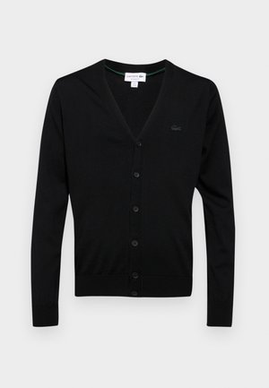 Cárdigan negro hecho de tejido de punto, con cuello en V, botones frontales y un pequeño parche con el logotipo en el lado izquierdo. Textura suave, diseño ajustado.