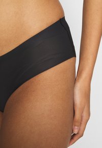 Fekete bikini alsó sima, rugalmas anyagból készült. Alacsony derekú szabása és minimális varrása van a szélek mentén, ami letisztult megjelenést kölcsönöz.