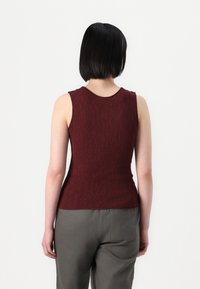 Top fără mâneci, de culoare burgundă, cu material texturat, decolteu rotund și croială ajustată, asortat cu pantaloni gri cu detalii la buzunarul din spate.