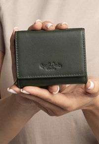 Dark green leather wallet with a smooth texture, featuring a fold-over flap and embossed logo. Held in hands against a neutral background.