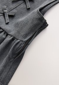 Gråt denimstof med samlet tekstur, med en sides lynlås og dekorative sløjfer, fokus på en glat finish og detaljerede syninger.