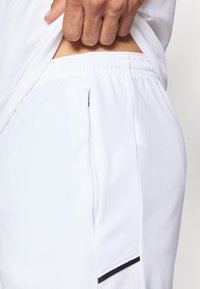 Λευκά αθλητικά σορτς με υφασμάτινη υφή που επιτρέπει την αναπνοή και ελαστική μέση. Πλάγια τσέπη με φερμουάρ.