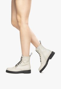 Witte leren enkelboots met een vetersluiting aan de voorkant en een zijrits, met een zwarte rubberen zool en een lus als trekhaak aan de hiel.