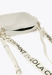 Borsa a tracolla rettangolare color avorio con una cerniera parzialmente aperta e una tracolla regolabile, caratterizzata da testo nero e simboli a cuore.