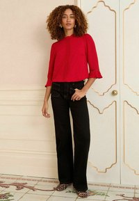 Blusa rossa con maniche a sbuffo e decorazioni, abbinata a jeans neri a vita alta e ballet flats con stampa animale su piastrelle a motivi.