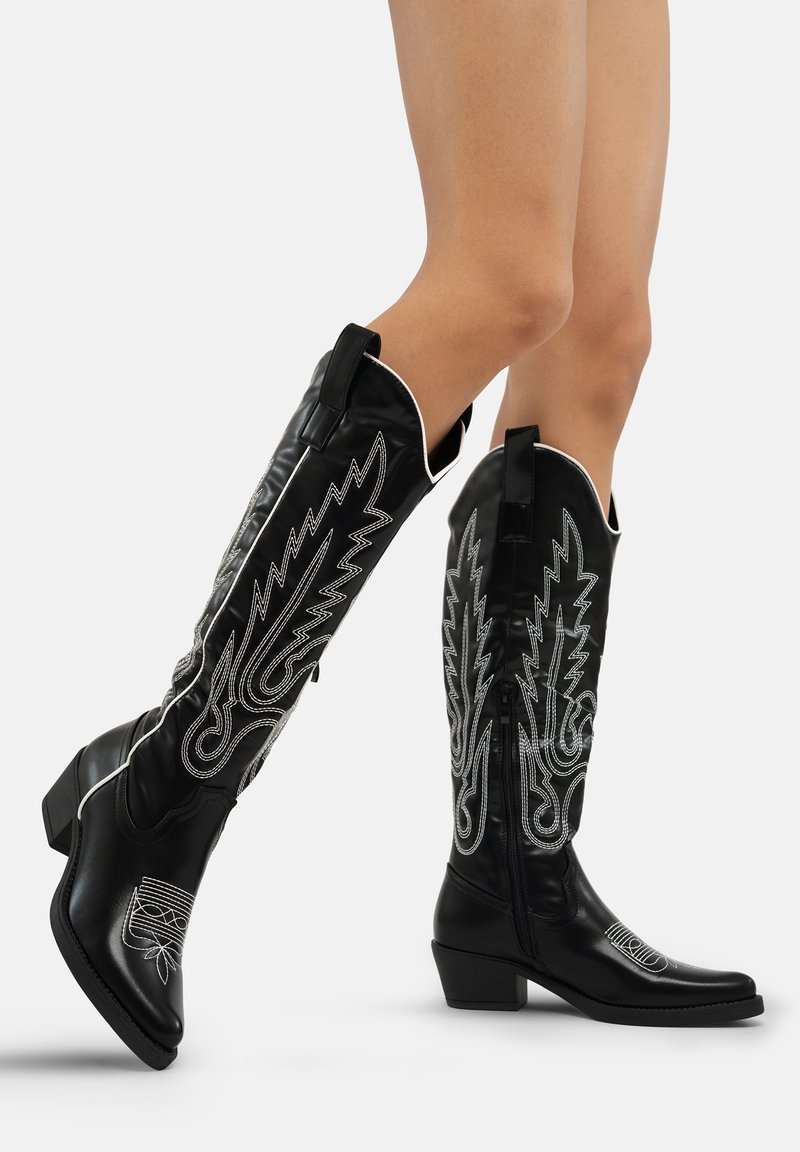 Botas de cuero negro hasta la rodilla con bordado plateado, punta redonda, tacón bajo y tirador. Cierre con cremallera en el lado.