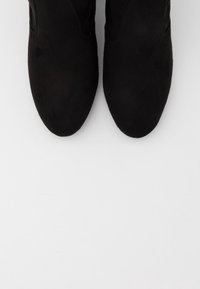 Bottes chevilles en daim noir à texture lisse, bout pointu et panneaux latéraux élastiques pour un enfilage facile. Semelles plates pour parfaire le design.