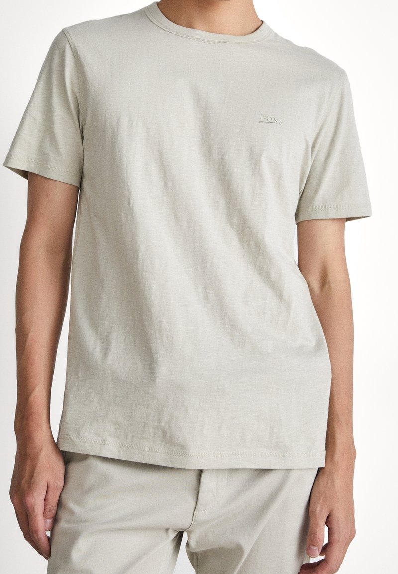 Helle graue Baumwoll-T-Shirt mit Rundhalsausschnitt, kurzen Ärmeln und dezentem Logodetail auf der Brust. Sanfte Textur und lässige Passform.