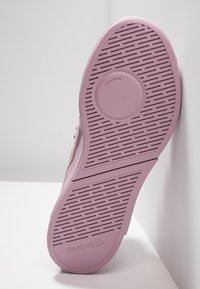 Sula på en rosa Reebok-sneaker med texturerade greppmönster och en cirkulär "TURNZONE"-funktion, vilande mot en vit yta.
