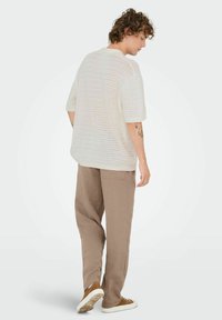 White knitted loose-fitting shirt with short sleeves and a textured pattern, paired with light brown tapered pants and brown sneakers.