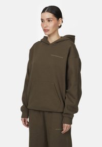 Hoodie oversize vert olive en mélange de coton, avec une poche avant, un capuchon à cordon de serrage et un détail de logo subtil au niveau de la poitrine.