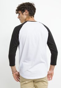 Schwarz-weißer Raglan-T-Shirt mit dreiviertel Ärmeln, aus Baumwolle gefertigt. Das Shirt hat einen Rundhalsausschnitt und eine glatte Textur.