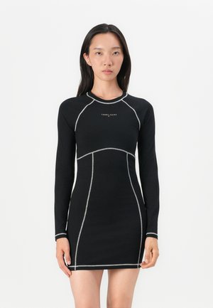 Robe noire à manches longues avec des coutures argentées et une silhouette ajustée, présentant un col rond et un logo de la marque sur la poitrine.