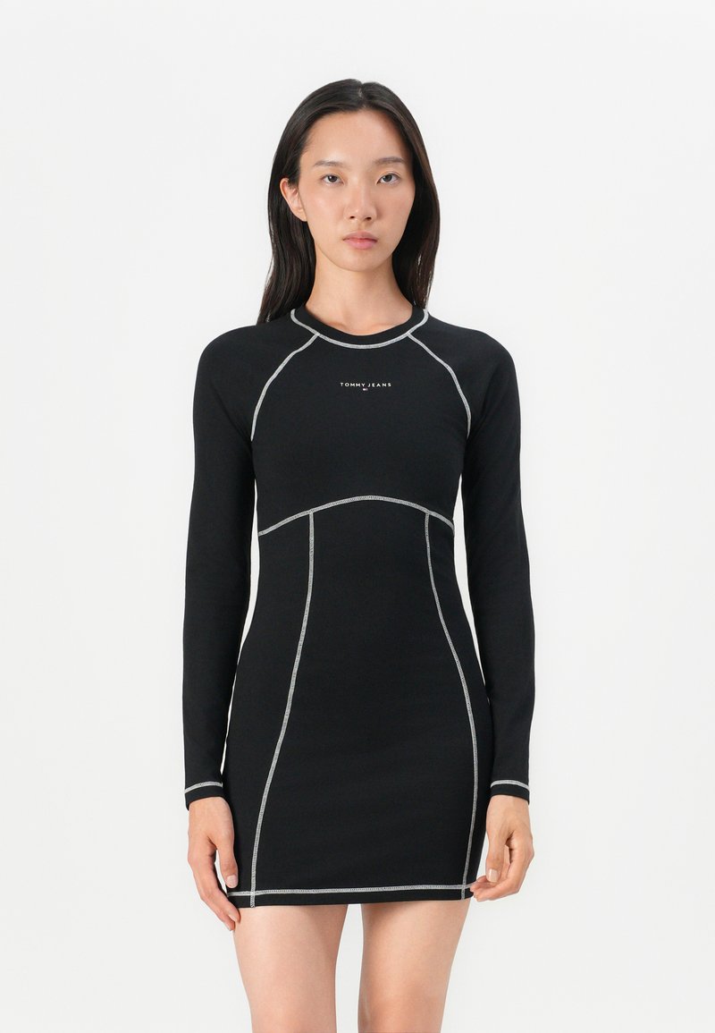 Robe noire à manches longues avec des coutures argentées et une silhouette ajustée, présentant un col rond et un logo de la marque sur la poitrine.