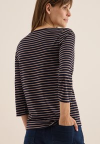 T-shirt à rayures bleu marine et beige, à manches longues, avec un col bateau et une coupe décontractée, présentant un ourlet incurvé et des fentes sur les côtés pour faciliter les mouvements.
