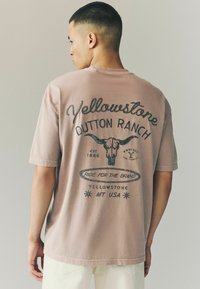 Kortærmet mauve t-shirt med trykt tekst og grafik, herunder et design af en oksehovedskelet, med en afslappet pasform og blød tekstur.