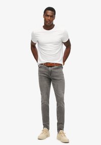Camiseta blanca de manga corta combinada con unos vaqueros gris ajustados. Un cinturón de cuero marrón y unas zapatillas de color beige claro completan el conjunto.