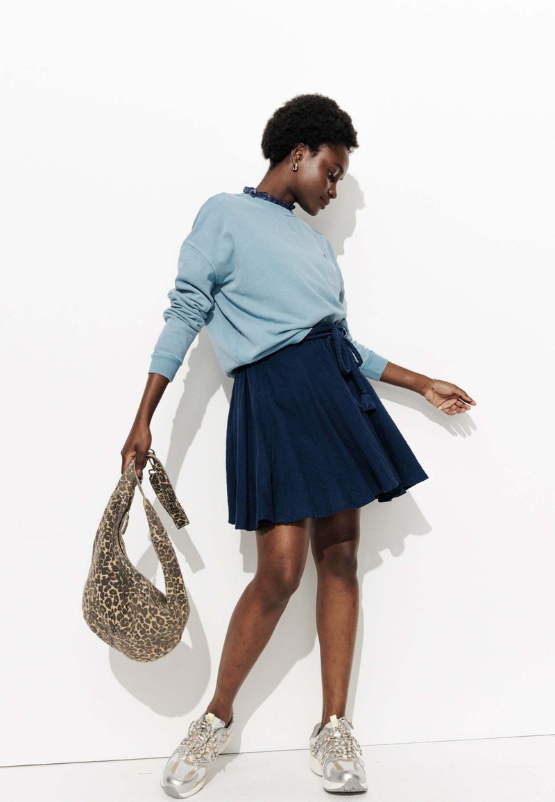 Sweatshirt bleu clair avec un col agrandi, associé à une jupe navy. Les accessoires comprennent un sac à imprimé léopard et des baskets argentées.