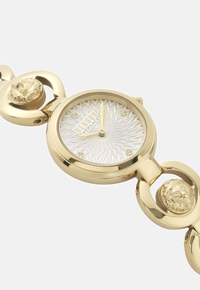 Reloj de oro con una esfera redonda, esfera plateada texturizada, acentos de cabezas de león en la correa y cuatro marcadores de diamantes en las posiciones de la hora.