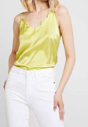 Camisole in satin verde lime con scollo a sbalzo, abbinata a jeans bianchi. La parte superiore presenta spalline sottili e una texture liscia e lucida.