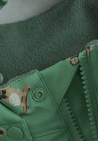 Grøn jakke med blødt fleecefor, trykknap- og lynlås-lukninger, samt et legende grafisk motiv af en hund på en skateboard.