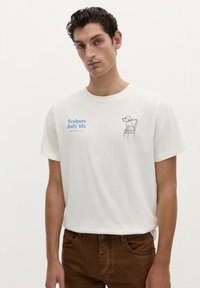 Weißes Baumwoll-T-Shirt mit kurzen Ärmeln, das einen blauen Textdruck mit der Aufschrift "Scalpers daily life" und eine Strichzeichnung eines Hundes auf einem Stuhl zeigt.