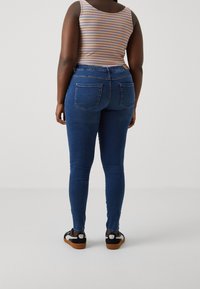 Höga blå denimjeans med en figurnära siluett, fyra fickor och sömmar längs benen. Matchas med svarta och vita sneakers.