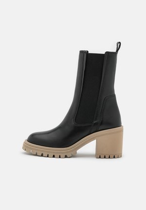 Black leather ankle boot with beige chunky block heel and thick treaded sole, elastic side panel, and pull tab at back.