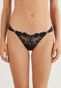 Zwarte kanten string met bloemenpatroon, voorzien van doorschijnend materiaal, gekartelde randen en verstelbare zijkooien met metalen accenten.