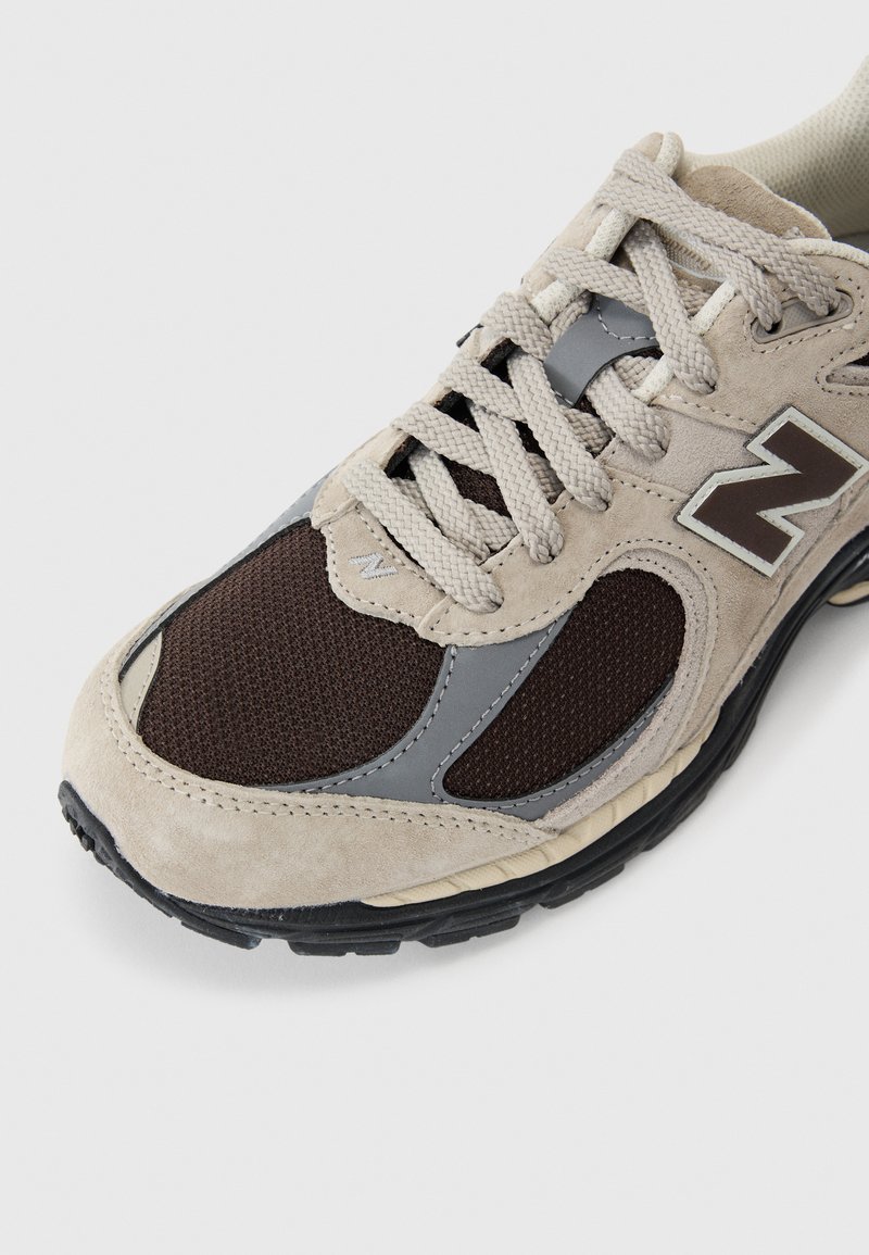 Beige and dark brown sneaker made of suede and mesh with gray accents. Features textured fabric, laces, and a black rubber sole.