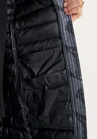 Zwarte geïsoleerde jasinterieur met een doorstikt ontwerp, glanzende afwerking en een klein zakje, met een contrasterende grijze voering.