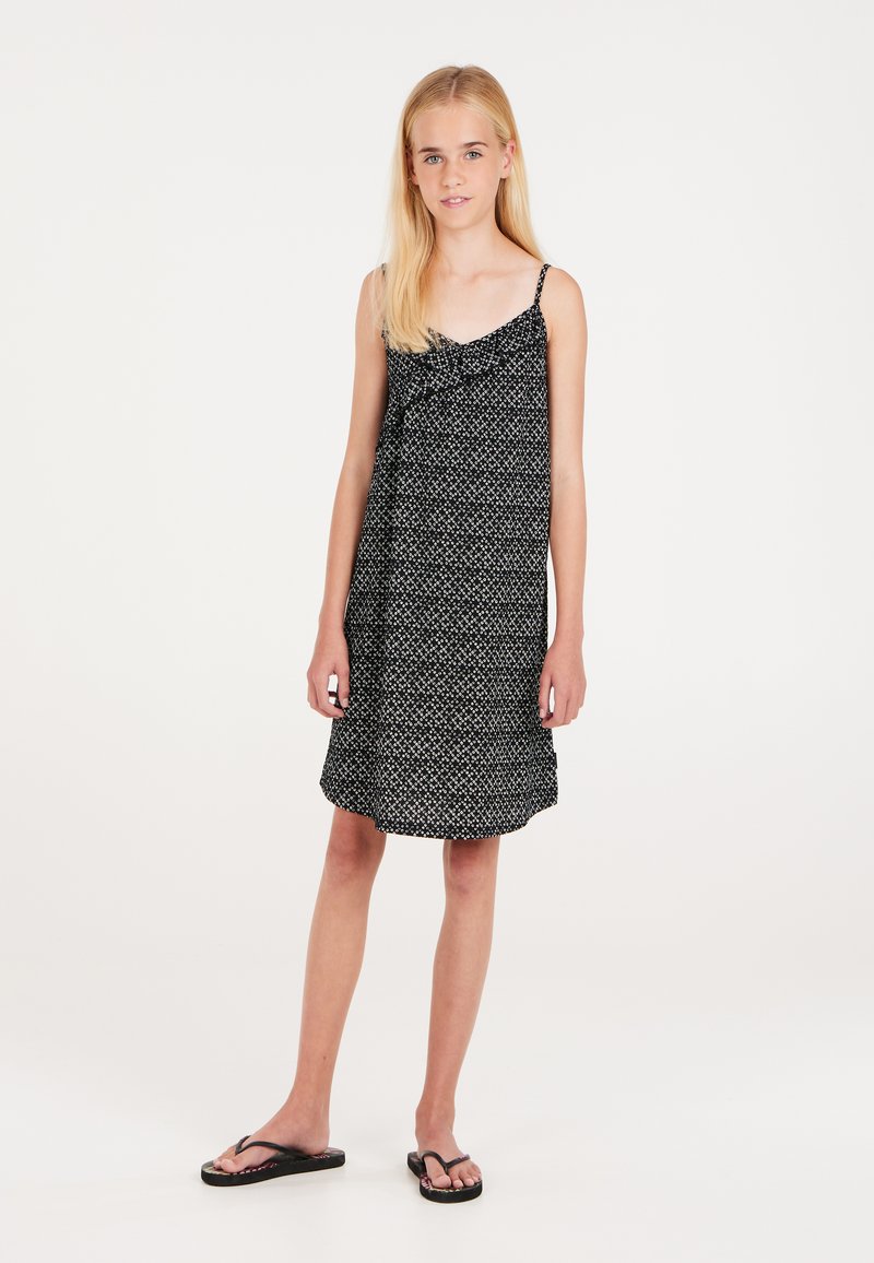 Robe noire sans manches avec un motif blanc subtil, en tissu léger, coupe droite et ourlet légèrement évasé. Associée à des tongs noires.